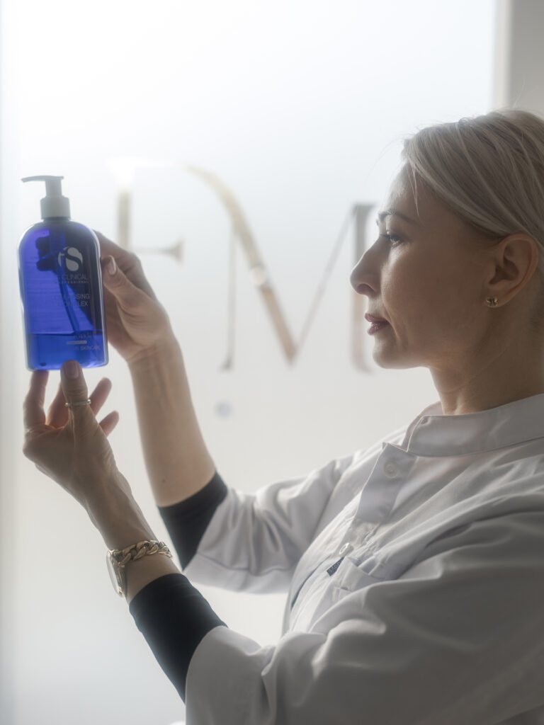 Frau laechelt, zeigt blaue Pumpeflasche, weisser Kittel, Schmuck